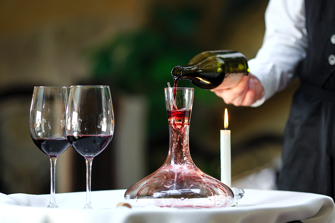 A sommelier pouring red wine into decanter